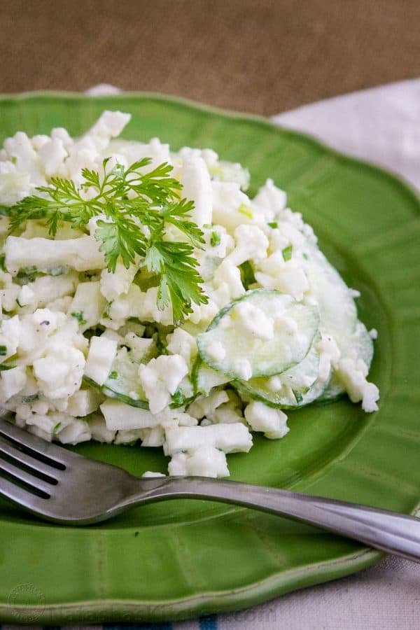 A green plate with cauliflower cucumber salad with a fork beside it 