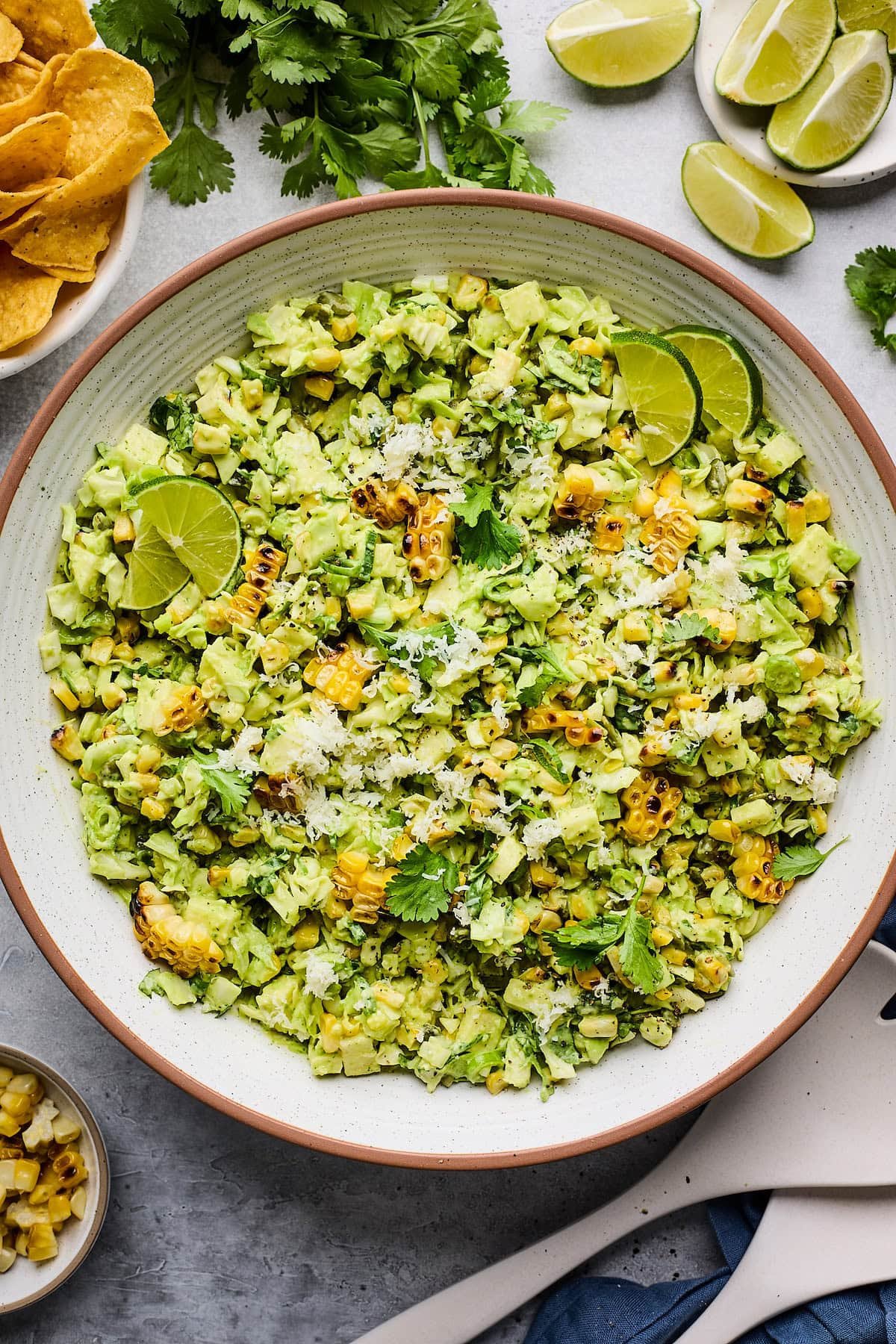 charred corn cabbage salad with creamy avocado dressing in serving bowl with lime wedges.