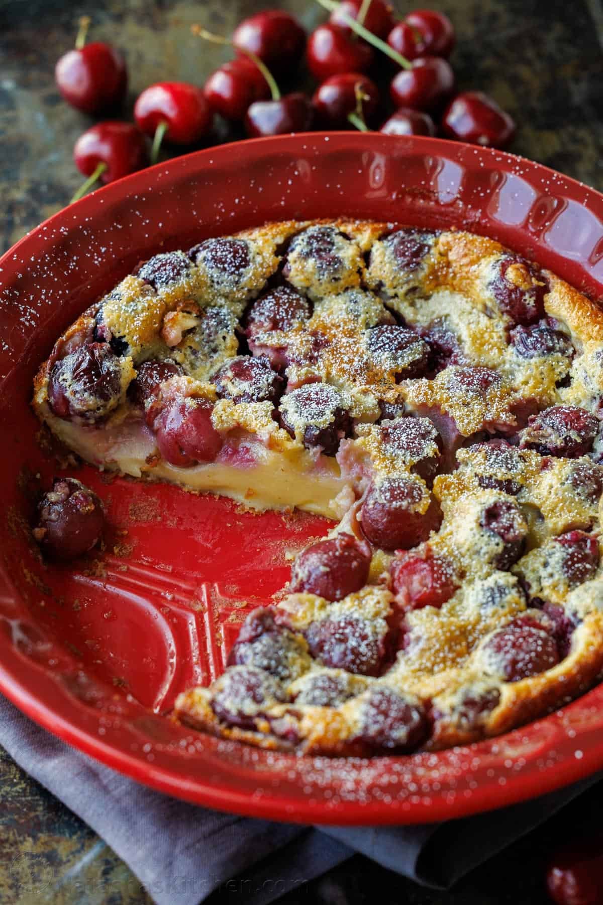 Cherry Clafoutis custard in a red dish with fresh cherries on the side