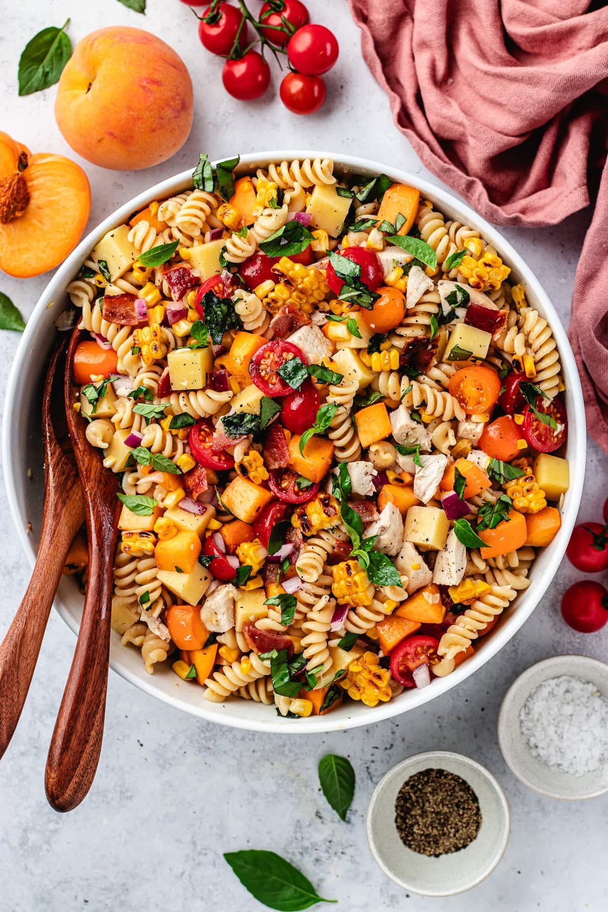 chicken bacon peach pasta salad with hot honey dressing in large serving bowl with salad servers.