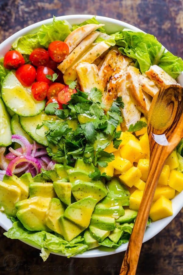Ingredients for chicken mango avocado salad arranged in bowl with spoon