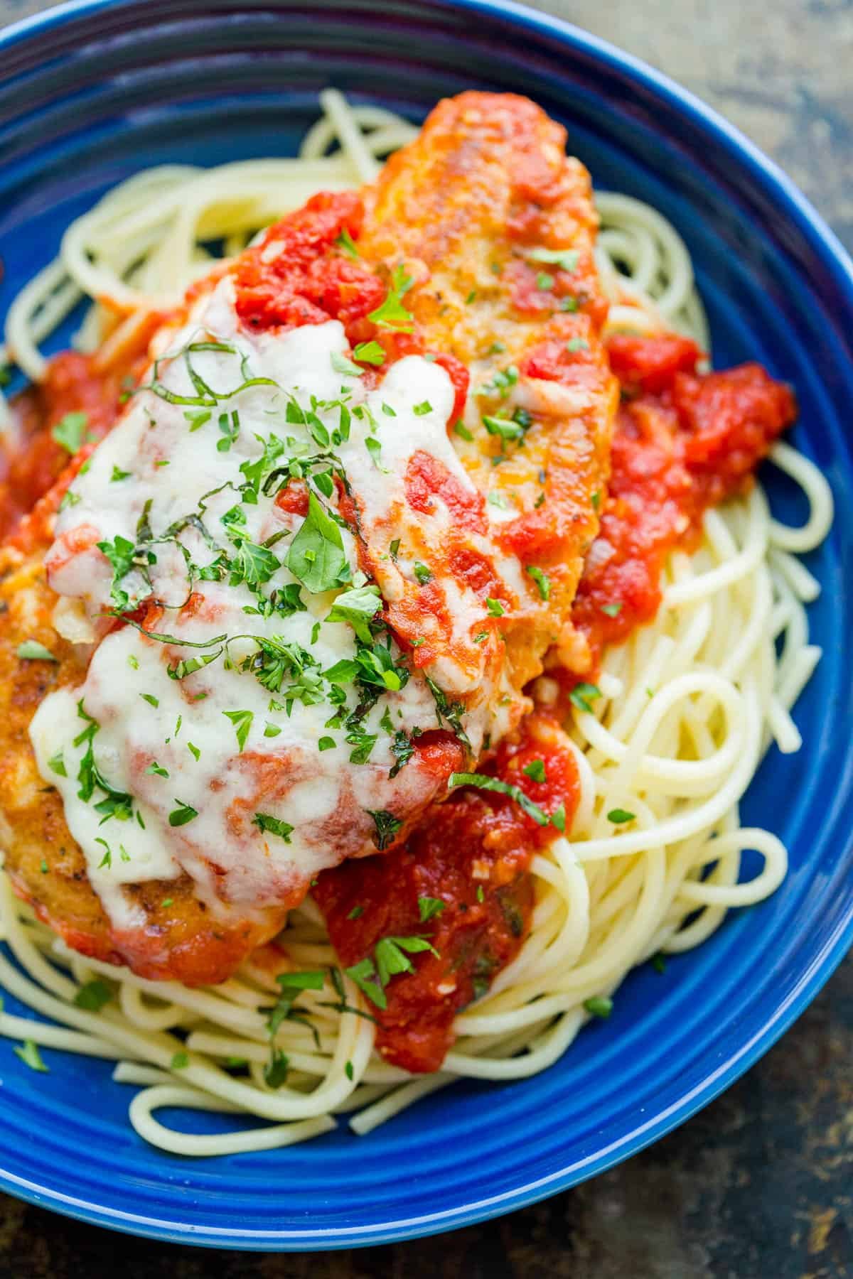How to make the best Chicken Parmesan with juicy chicken, crisp crust, topped with marinara and melty cheese - a classic restaurant remake! Chicken Parmesan served over pasta and marinara sauce, garnished with parsley