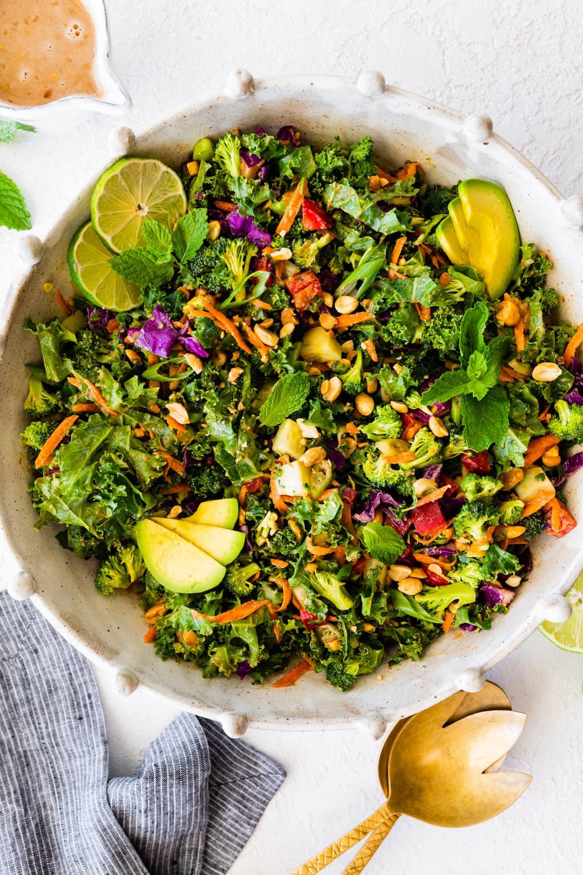 chopped kale broccoli salad with peanut dressing in bowl with avocado, peanuts, herbs, and lime.