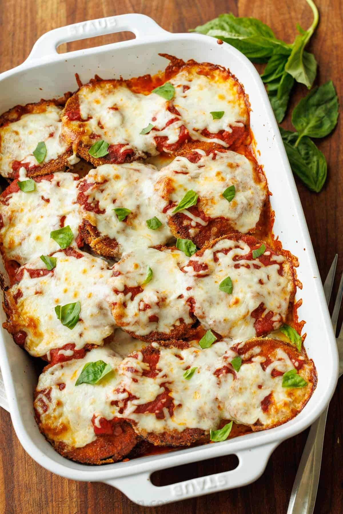 Eggplant Parmesan: Crispy breaded eggplant, layered with marinara sauce and mozzarella cheese, baked to perfection into a saucy and cheesy casserole. Eggplant parmesan in a baking dish, topped with mozzarella and fresh basil
