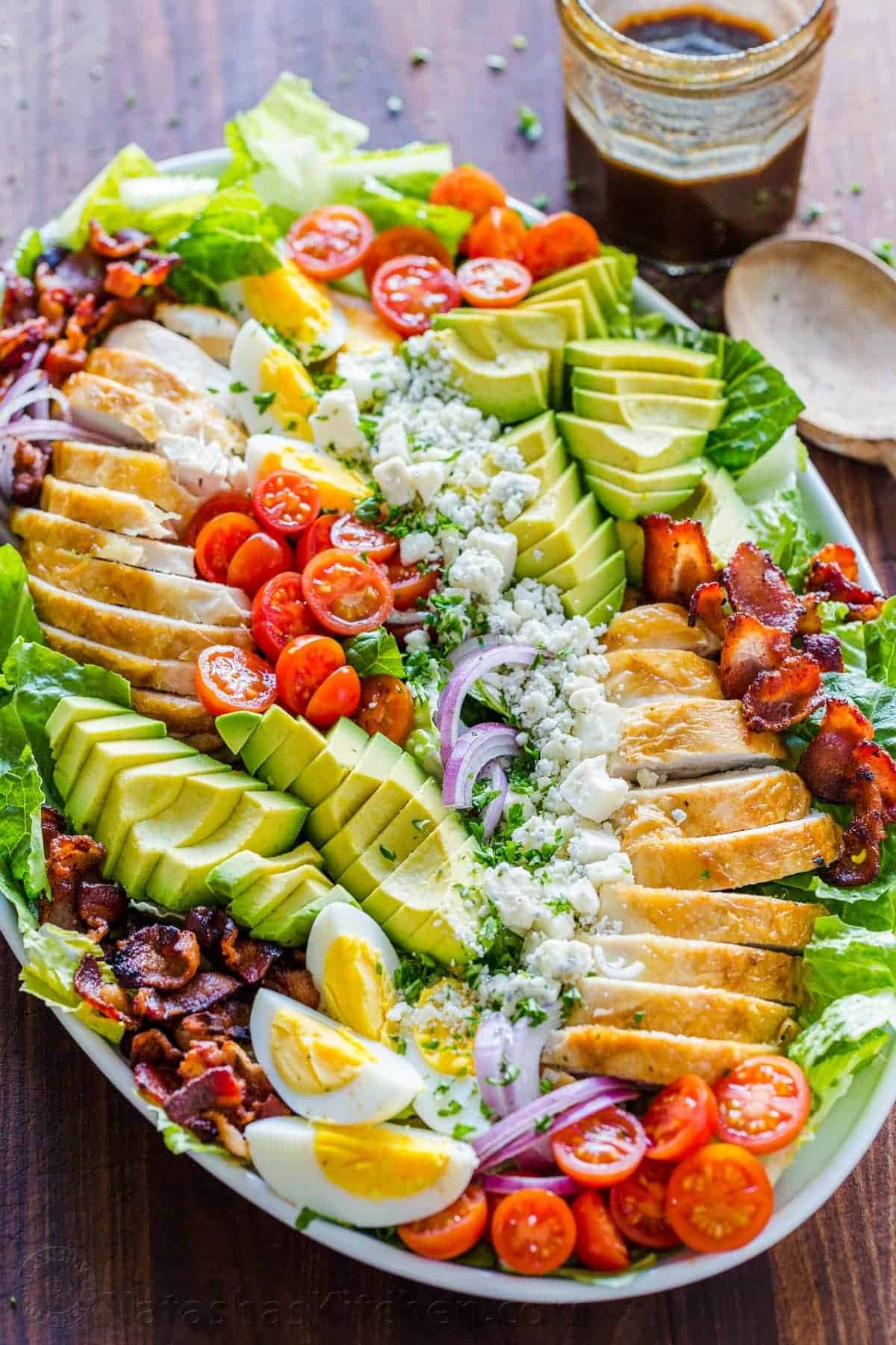 Easy Chicken Cobb Salad with the Best Cobb Salad Dressing! A protein-packed salad loaded with lettuce, tomatoes, chicken, avocado and cheese. Cobb salad on a platter with chicken, bacon, lettuce, avocado, tomatoes, blue cheese and dressing in a mason jar