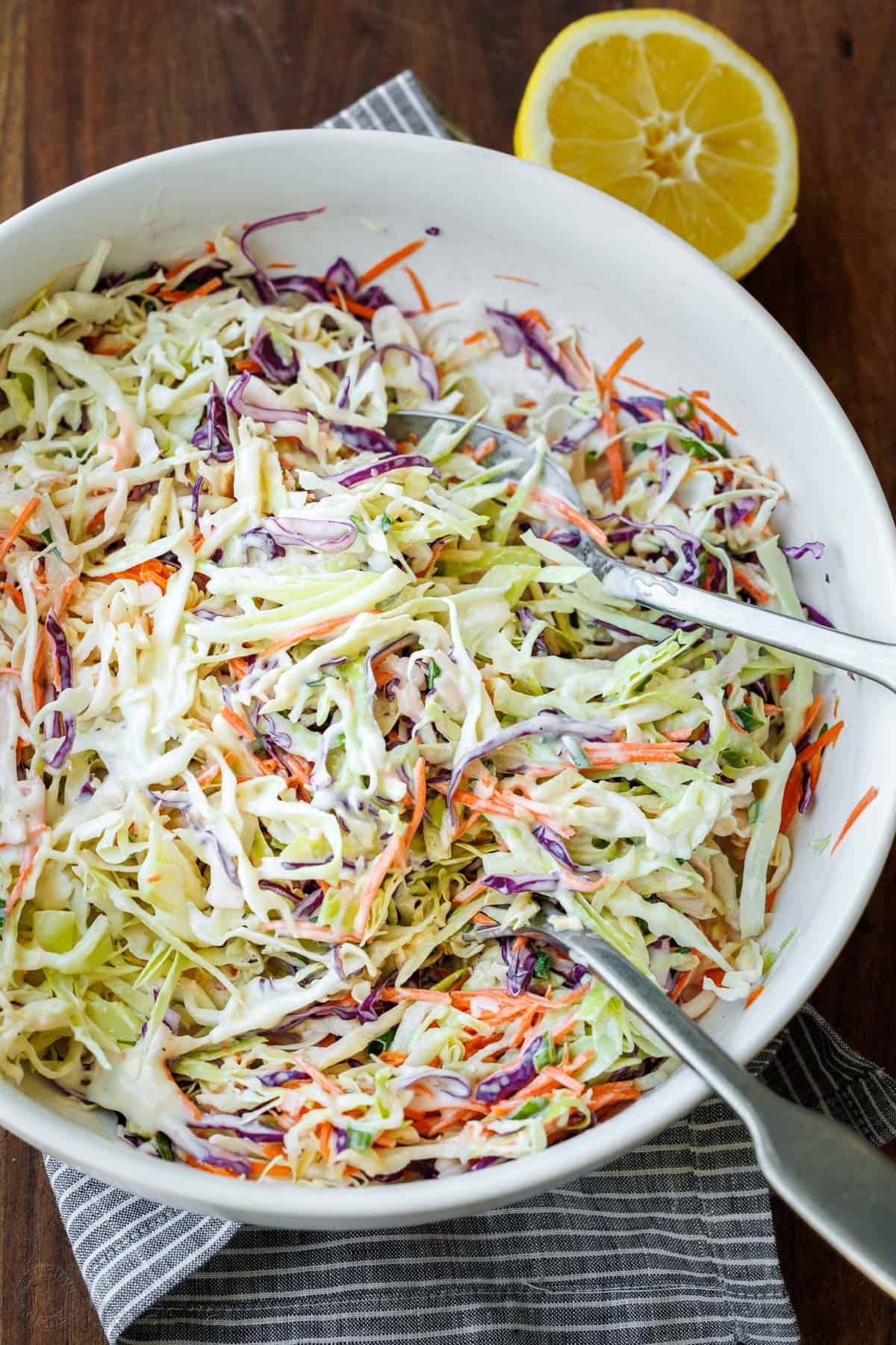 Classic Coleslaw with the best homemade coleslaw dressing. This creamy coleslaw is ready in 10 minutes and perfect for sandwiches, potlucks and cookouts. #coleslaw #coleslawrecipe #salad #sidedish #grillingside #homemadecoleslaw #coleslawdressing #natashaskitchen Homemade coleslaw with creamy dressing in a white bowl with serving spoon