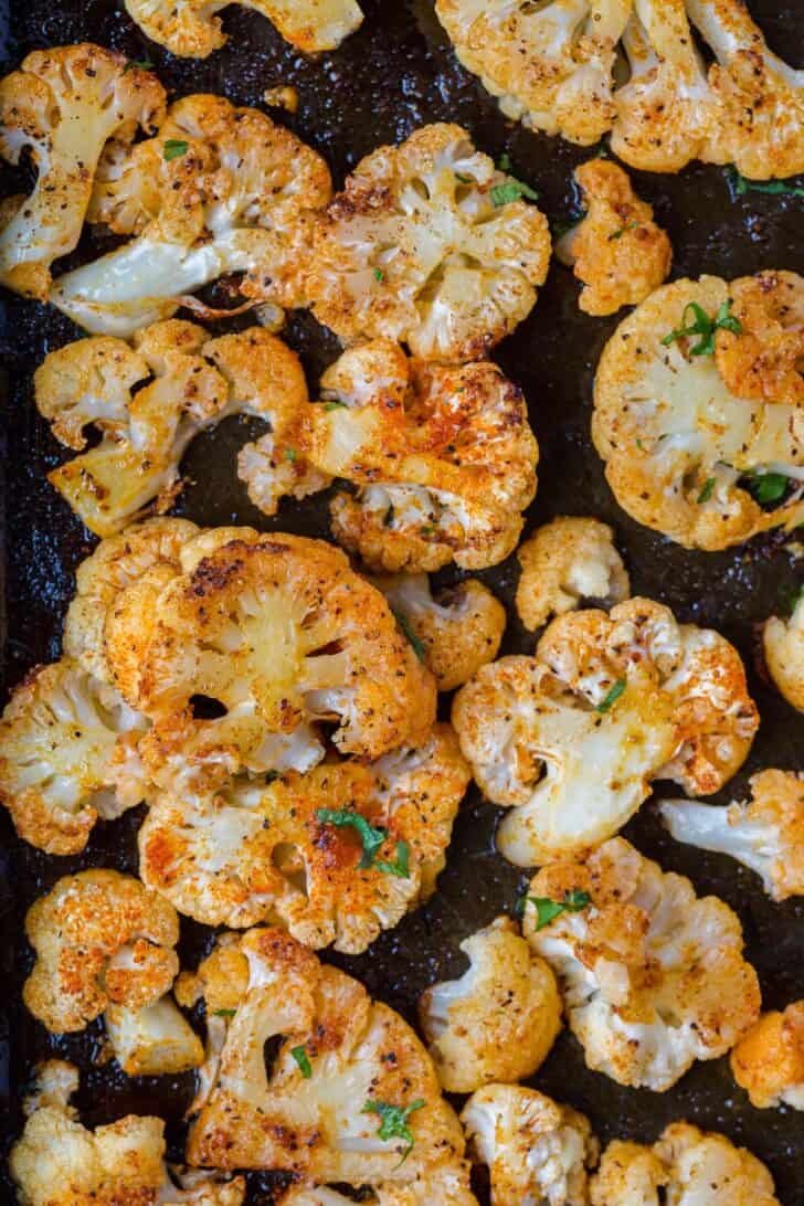 Our go-to roasted cauliflower recipe. How to bake or air fry cauliflower that's perfectly seasoned, tender, and golden. Roasted caulilfower florets on a baking sheet topped with fresh chopped greens.