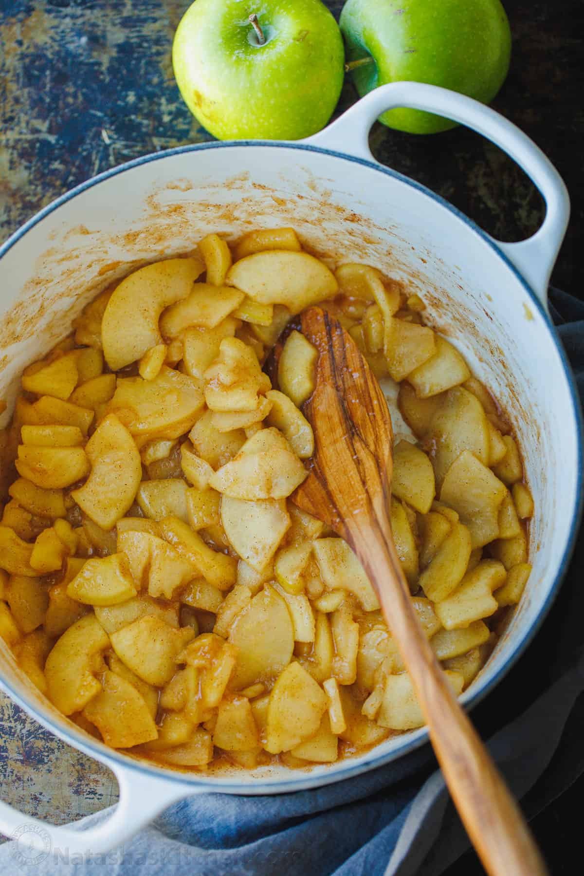 Easy sauteed cinnamon apples taste just like the filling in a cozy apple pie. Quick to make and perfect as a topping for breakfast or dessert. Sauteed cinnamon apples in a large pot with a wooden spoon.