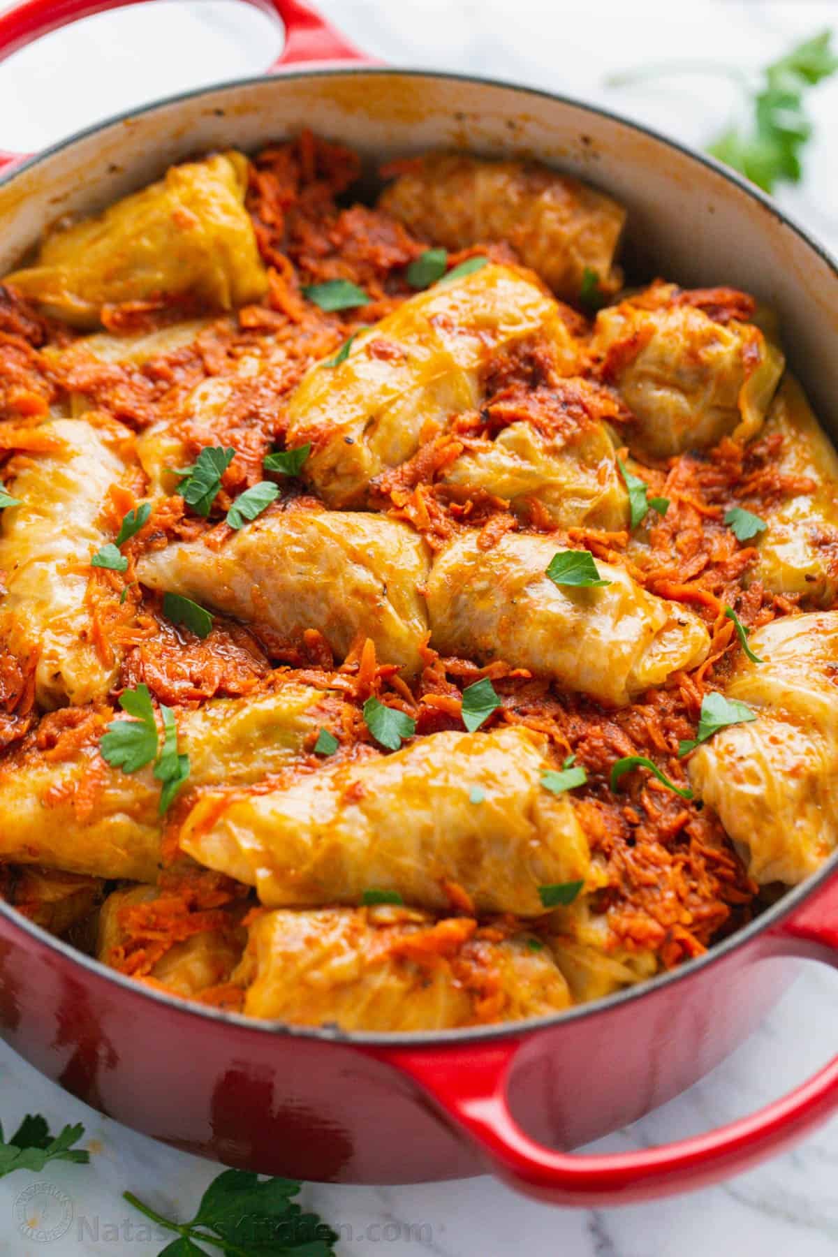 Stuffed cabbage rolls inside a red Dutch oven, covered in sauce.