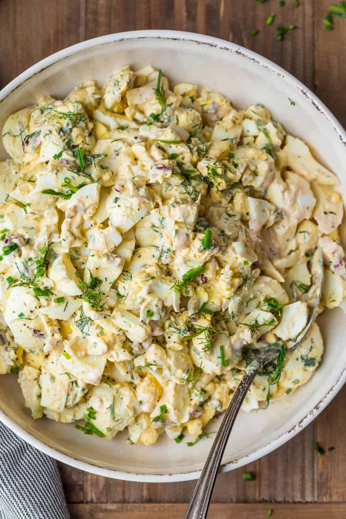 Truly the Best Egg Salad Recipe. Hard-boiled eggs with celery, dill, seasoning and chives in creamy dressing. Egg salad is a great way to use cooked eggs! Egg salad in a serving bowl with a spoon and topped with chives.