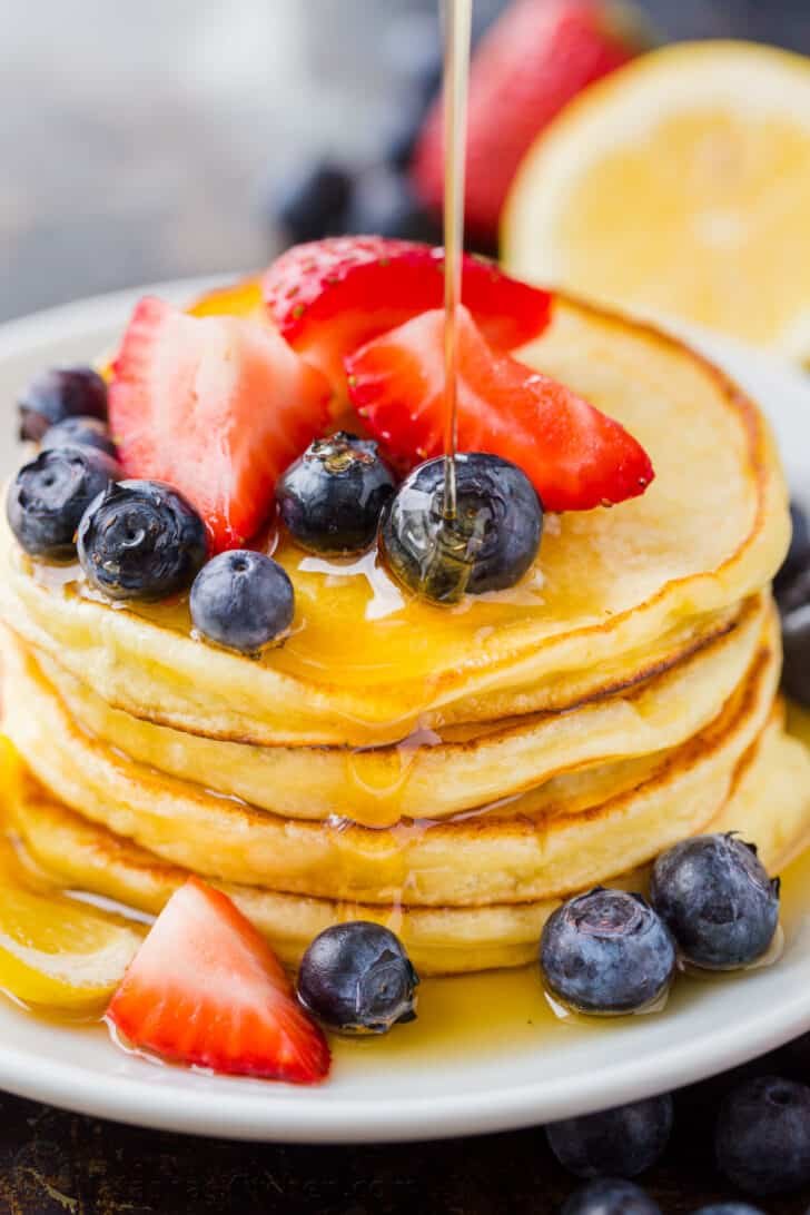 Ricotta Pancakes stacked on plate with fruit and drizzled with maple syrup