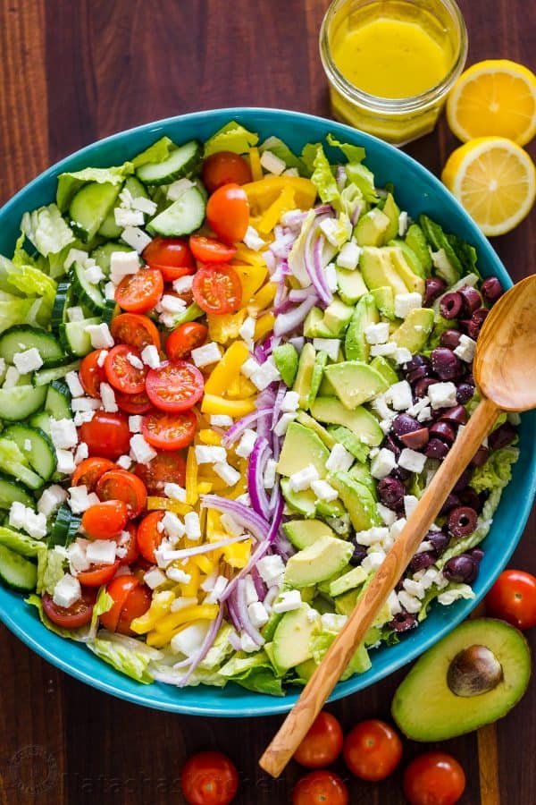 Fresh Greek Salad is a must try! So healthy with cucumber, tomato, avocado, olives and feta. You will want the easy Greek dressing on all of your salads! Greek Salad Recipe in a bowl with Greek dressing on the side