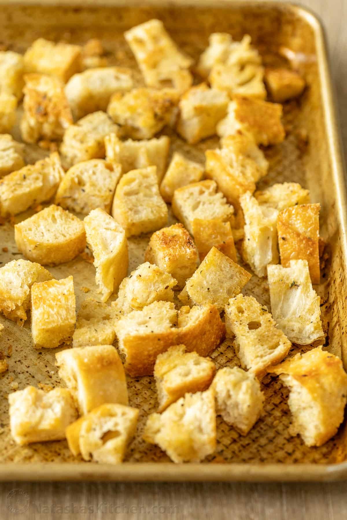 Turn day-old bread into crunchy homemade croutons! Toss these oven-baked garlic croutons over a Caesar salad or snack on them by the handful. Homemade croutons on a metal baking sheet.
