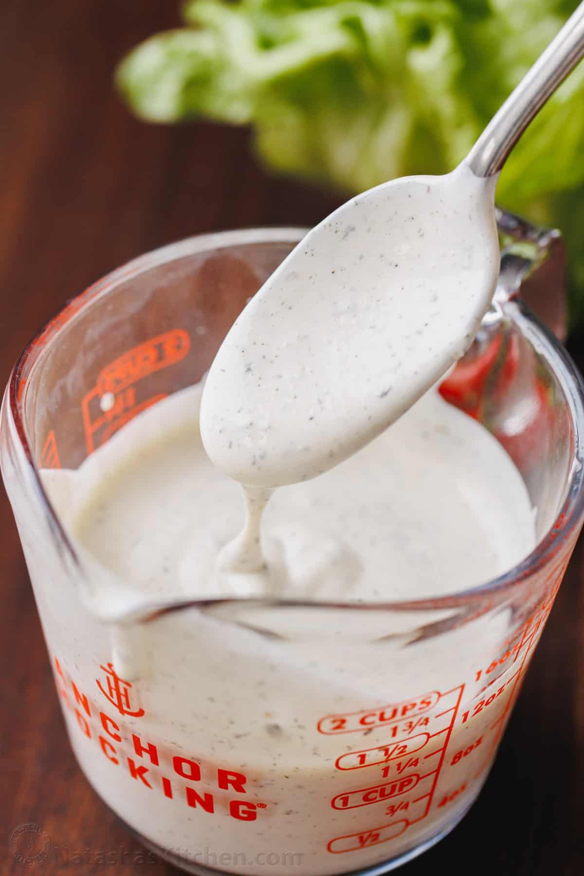 Make restaurant-style buttermilk Ranch Dressing in seconds! This creamy homemade ranch recipe is perfect as a salad dressing or as a dip. A spoon drizzles ranch dressing into a measuring cup.