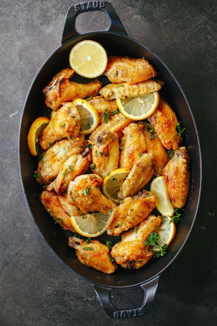 Baked Lemon Pepper Wings are crispy outside and tender inside. These chicken wings are coated in an irresistible lemon pepper butter sauce. Baked Lemon Pepper Wings in a serving tray with lemons.