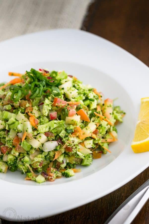 A bowl of loaded broccoli radish salad with a slice on lemon beside it 