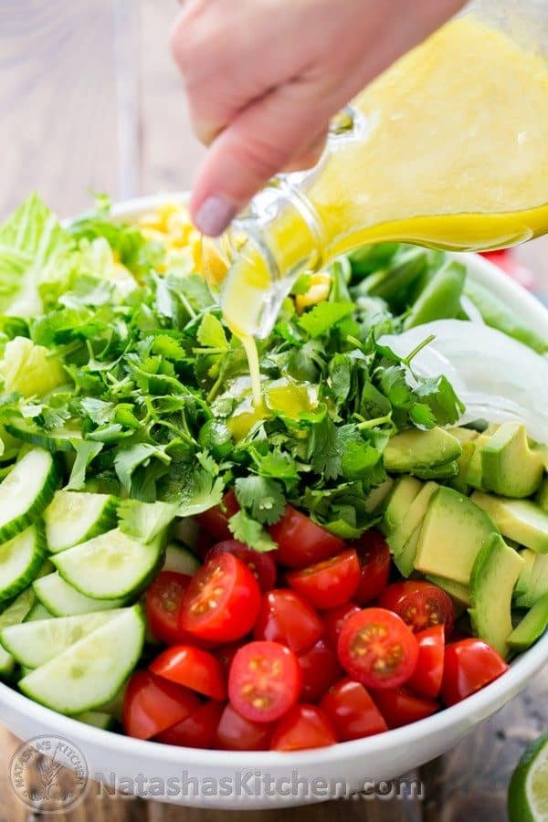 A bowl of Mexican salad with a lime dressing being poured over the salad