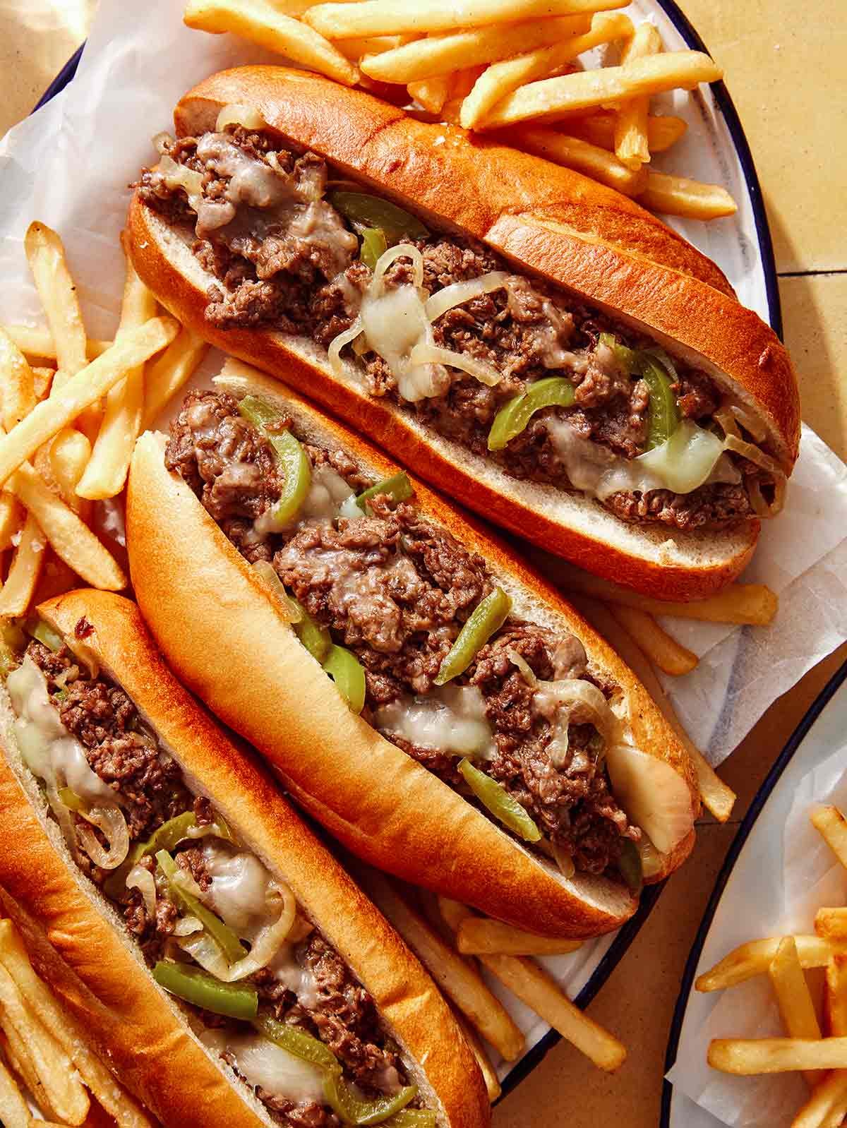 A platter of Philly Cheesesteak sandwiches with fries next to it.