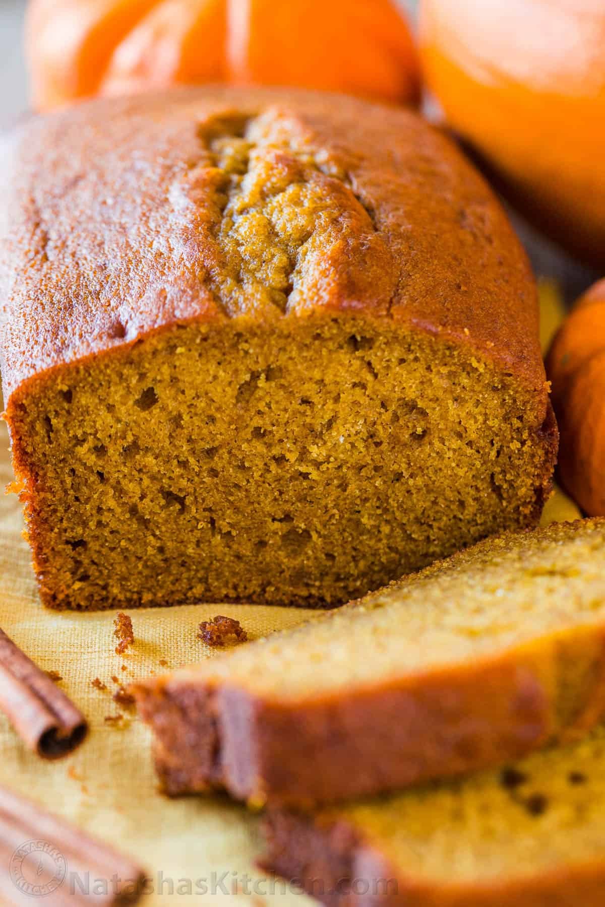 Pumpkin Bread has a soft and moist crumb with wonderful pumpkin flavor. This is our go-to easy pumpkin bread recipe and it's freezer friendly! #pumpkinbread #pumpkinbreadrecipe #easypumpkinbread #pumpkin #pumpkinrecipes #thanksgiving #dessert #bread Sliced pumpkin bread with pumpkins in background