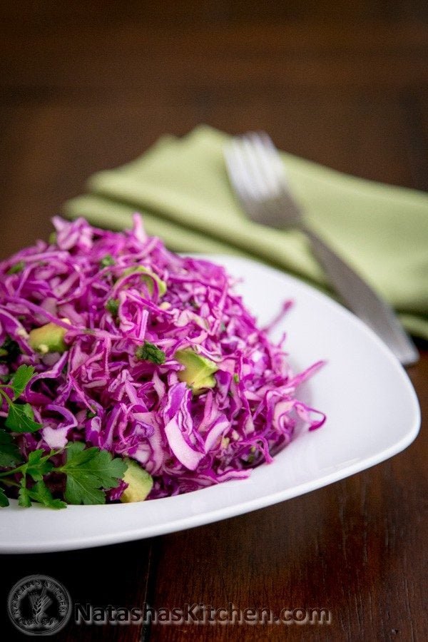 A plate of red cabbage and avocado salad with a fork and cloth napkin beside it 