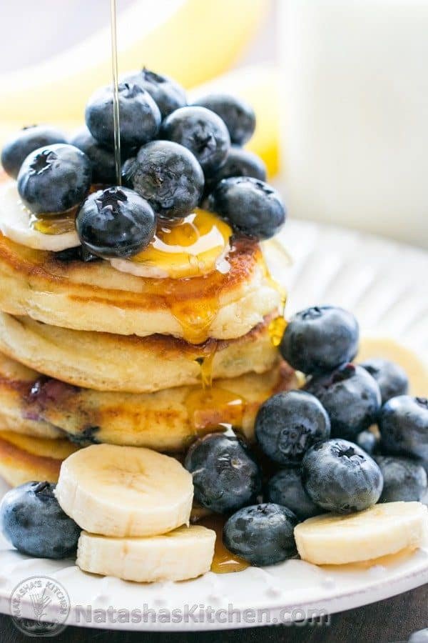 Stack of sour cream blueberry pancakes topped with syrup, blueberries, and bananas.