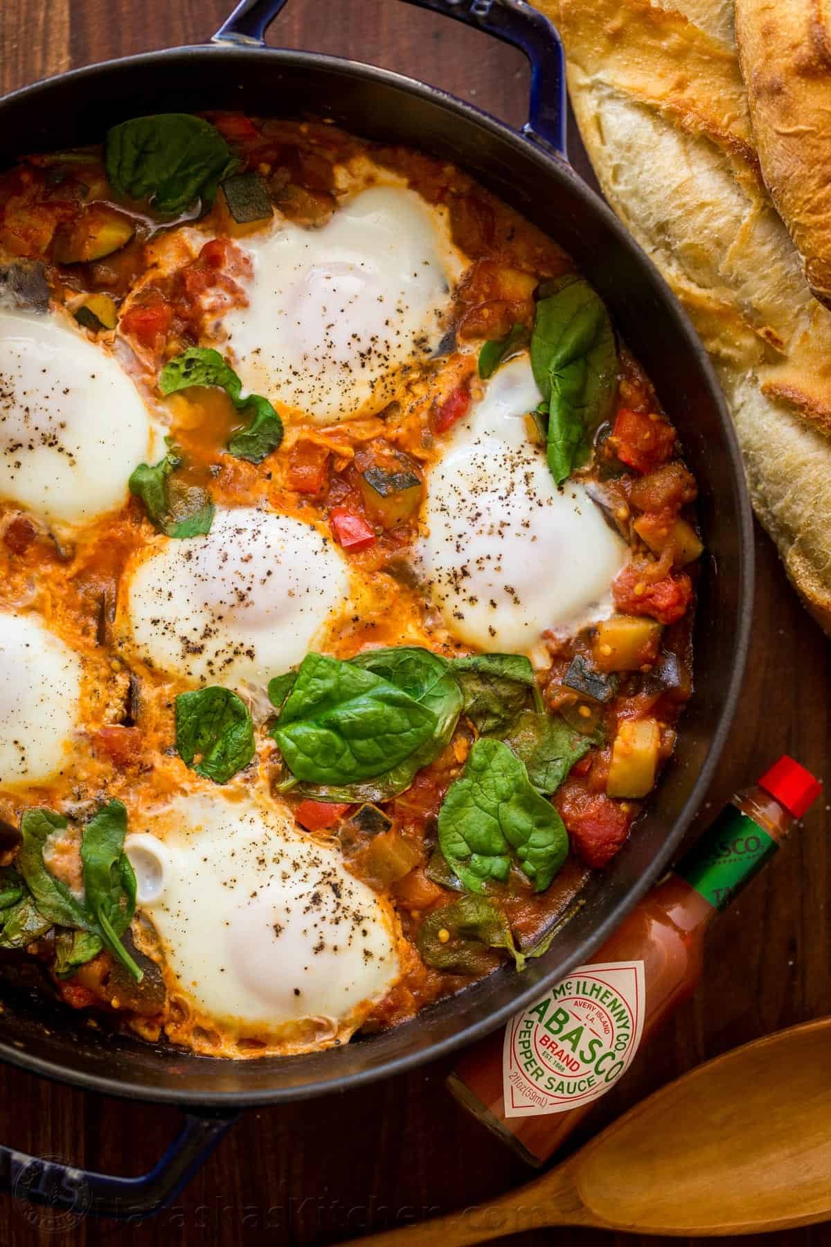This Eggplant Shakshuka is loaded with zucchini and eggplant in a spicy tomato-based sauce, crowned with egg and fresh spinach. Eggplant Shakshuka served in a skillet with bread