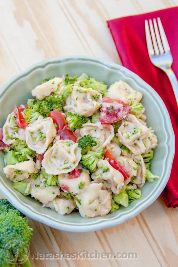 A bowl of tortellini salad with red, cloth napkin with a fork on top beside it 