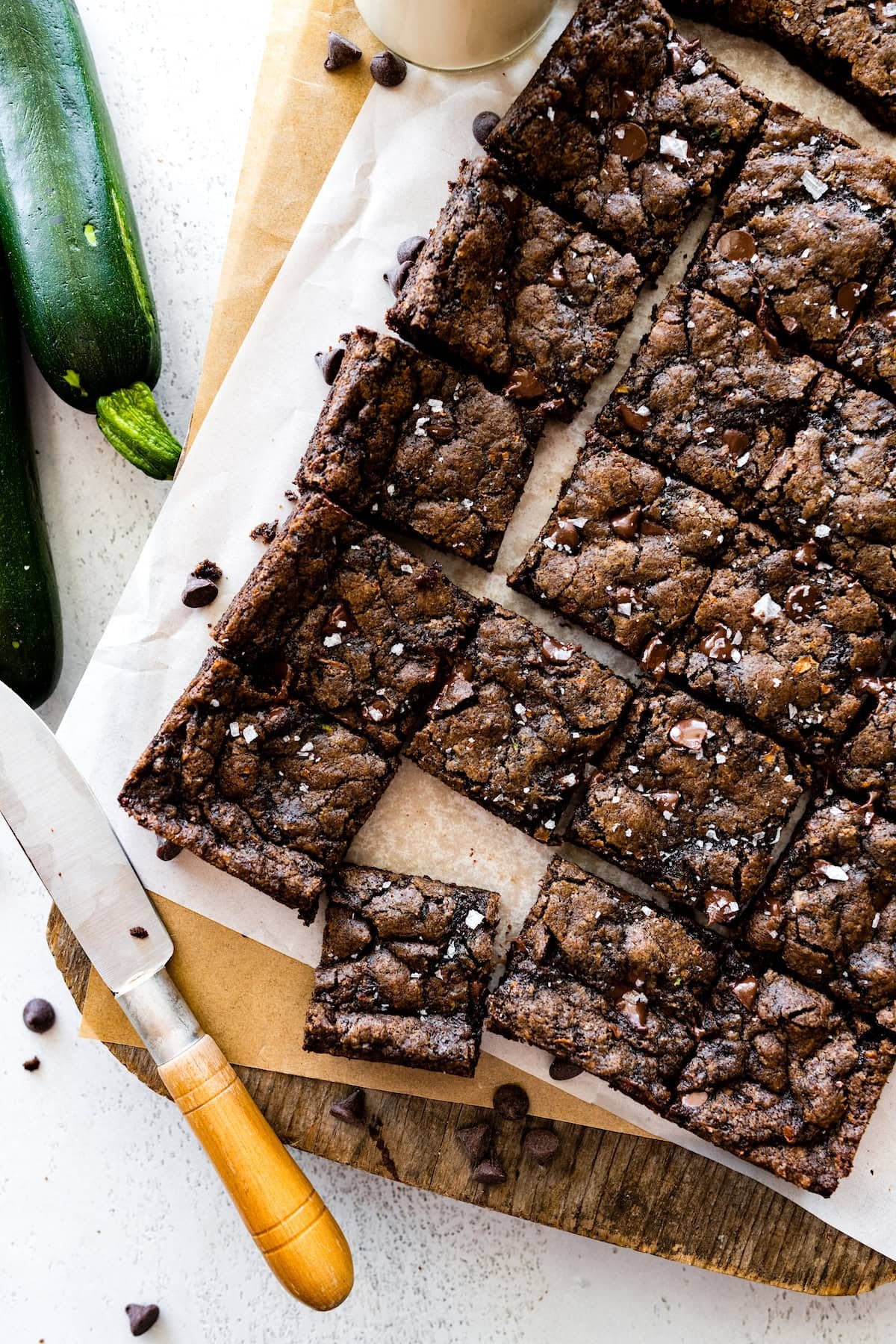 zucchini brownies cut into squares on wood board with knife. 