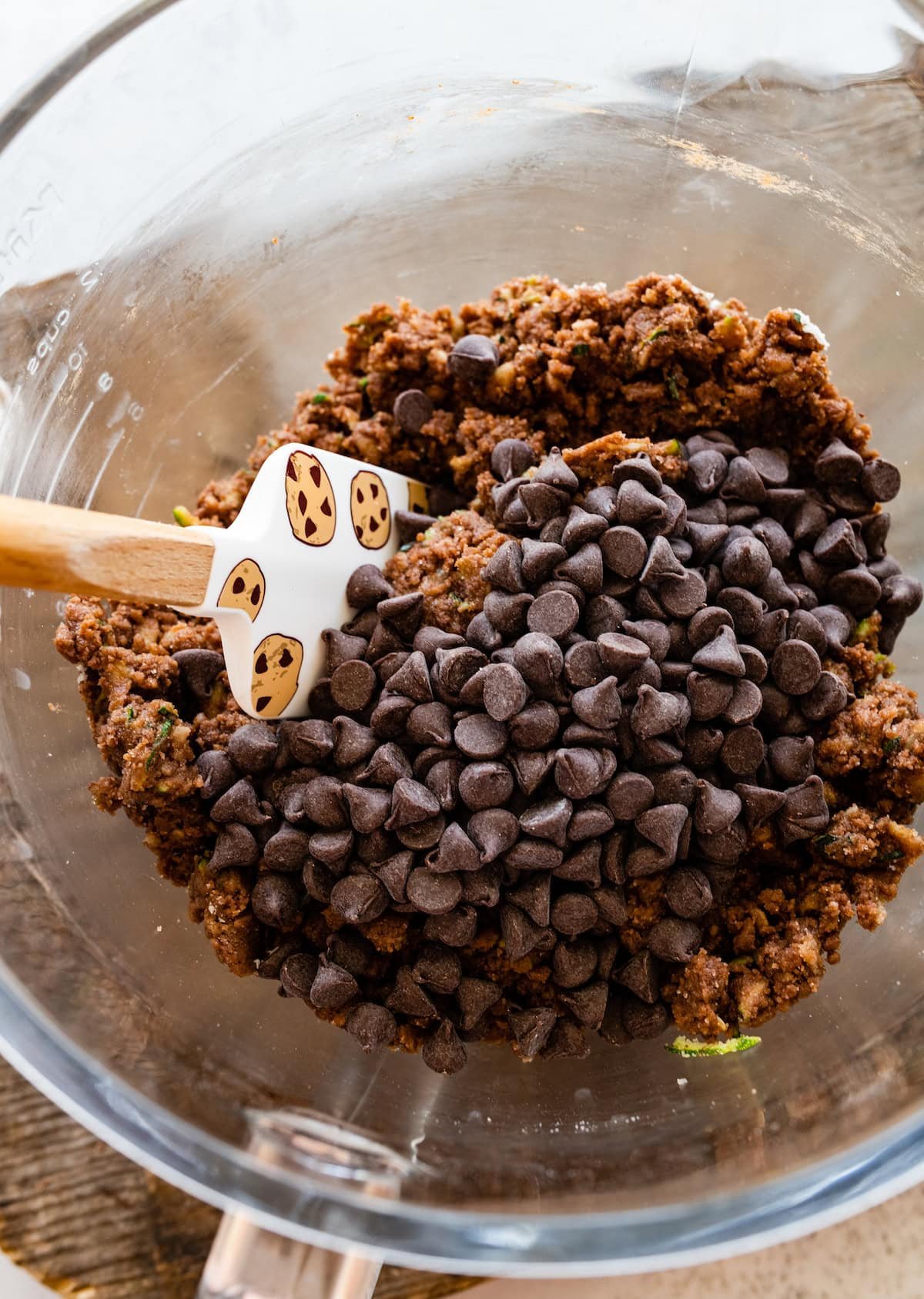 zucchini brownie batter with chocolate chips in mixing bowl with spatula. 