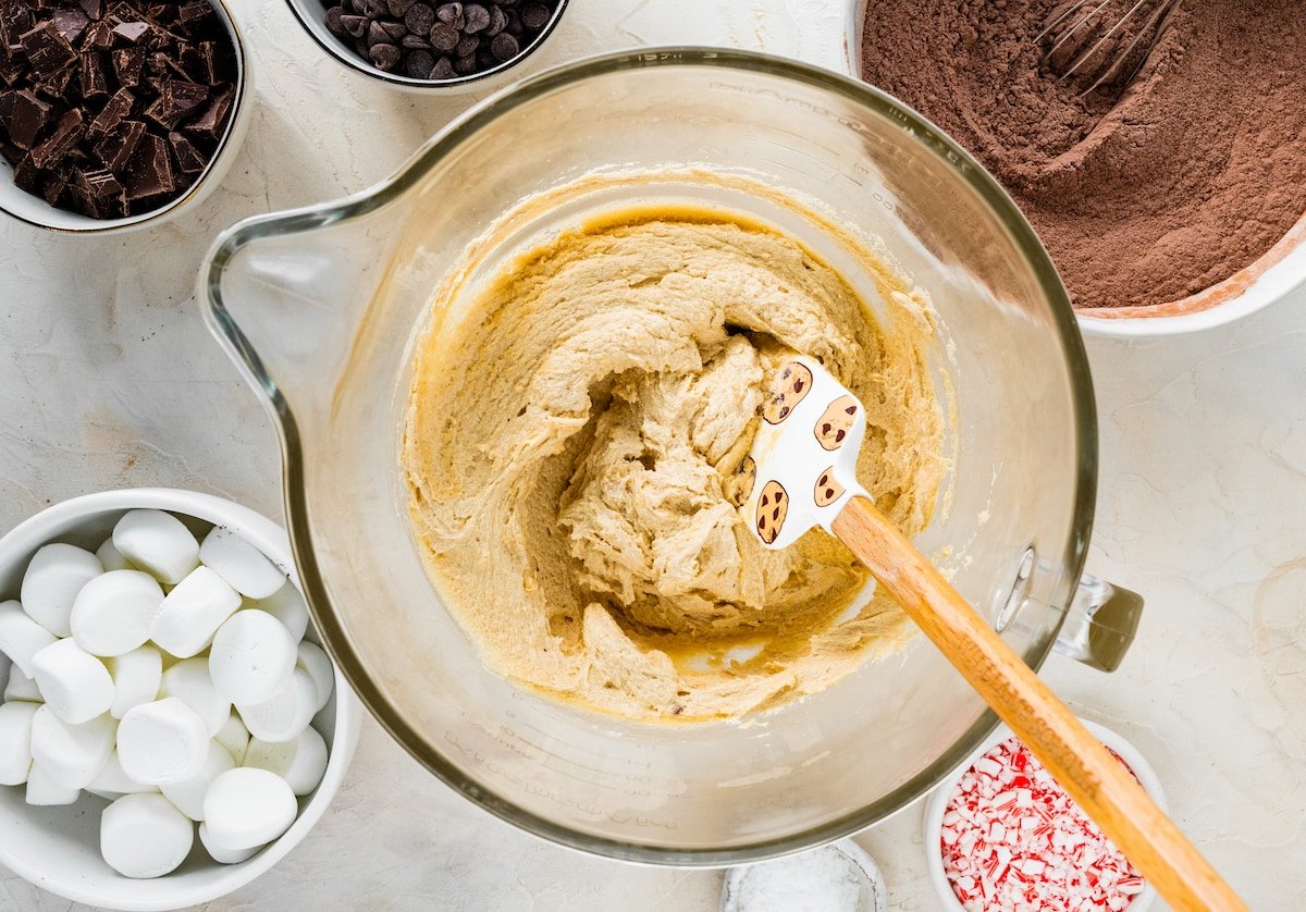 butter, sugars, eggs, vanilla, and peppermint extract mixed together in mixing bowl with spatula.