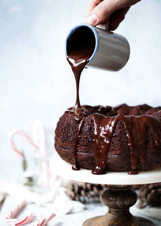 Chocolate glaze being poured over Chocolate Peppermint Bundt Cake on cake stand. 