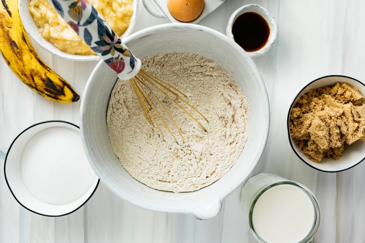 whisking dry ingredients together in mixing bowl to make banana cake. 