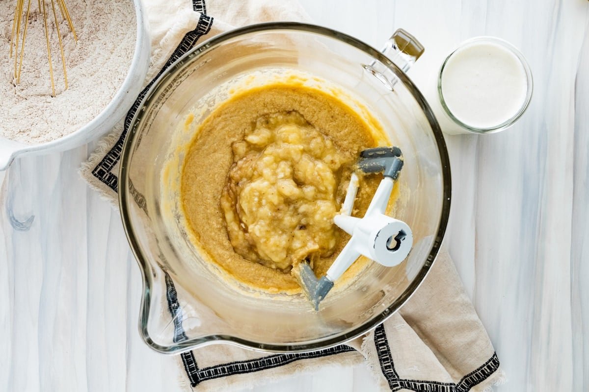 mashed bananas being added to cake batter in mixing bowl. 