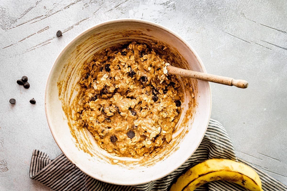 breakfast cookie dough with oats, chocolate, chips, and raisins in mixing bowl with wooden spoon.