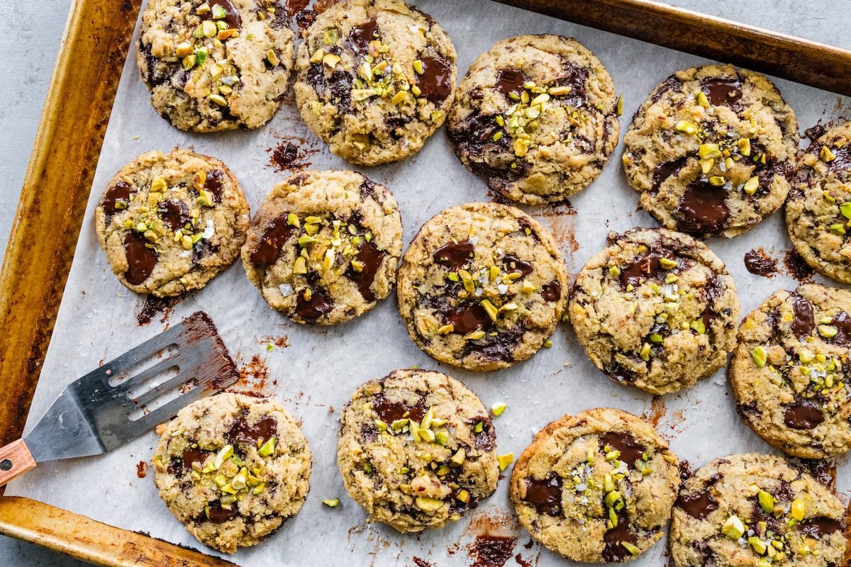 dark chocolate chunk pistachio cookies on baking sheet with parchment paper and spatula.
