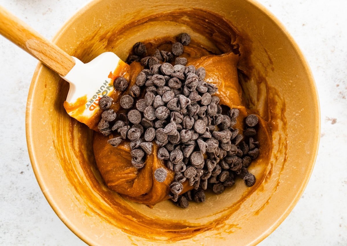 flourless peanut butter blondie batter with chocolate chips in mixing bowl with spatula.