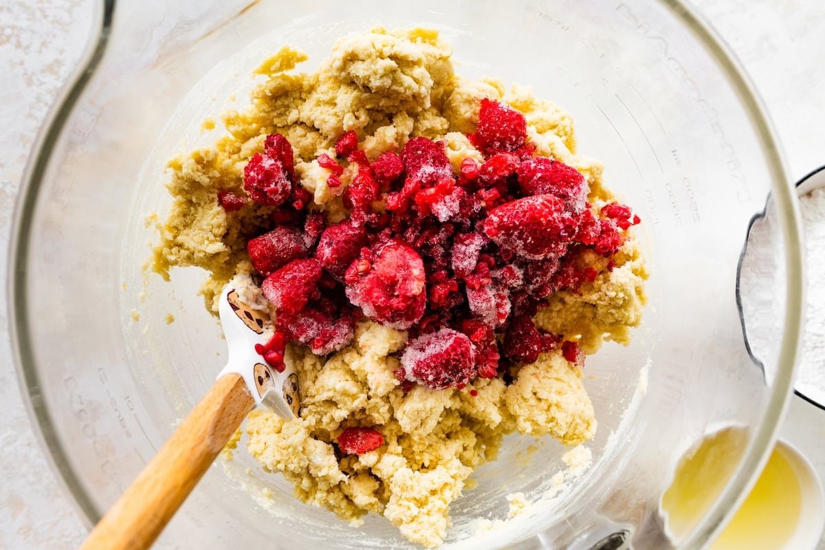 frozen raspberries being folded into lemon cookie dough in mixing bowl.