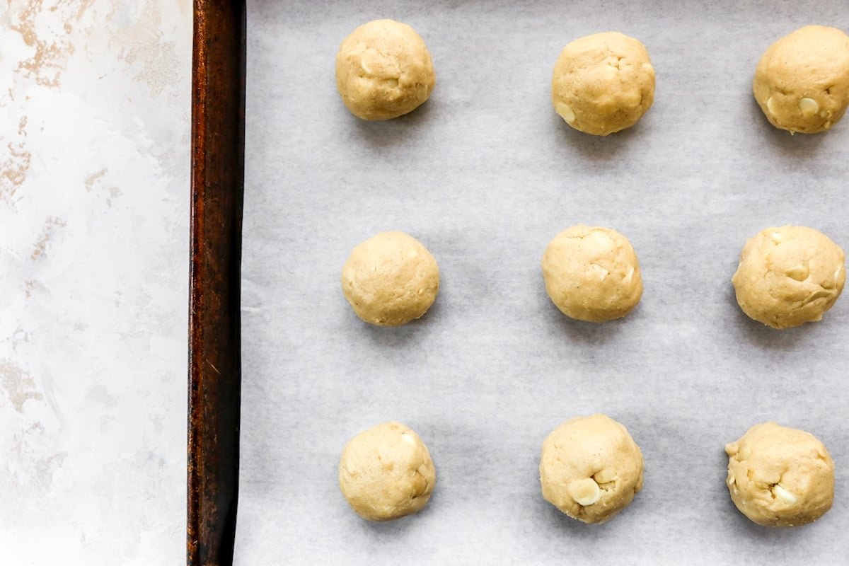 white chocolate macadamia nut cookie dough balls on baking sheet with parchment paper.