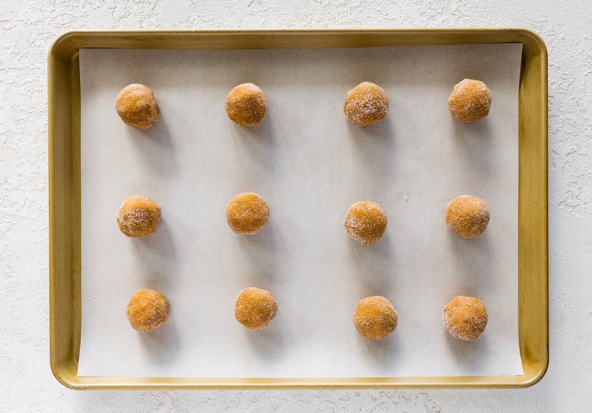 ginger molasses rolo cookie dough balls rolled in sugar and on baking sheet with parchment paper.