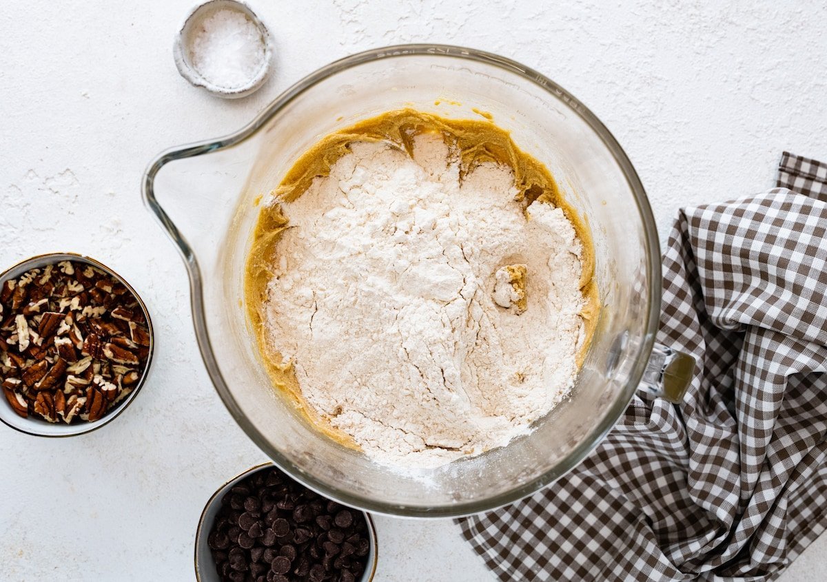 adding flour to cookie dough in glass mixing bowl.