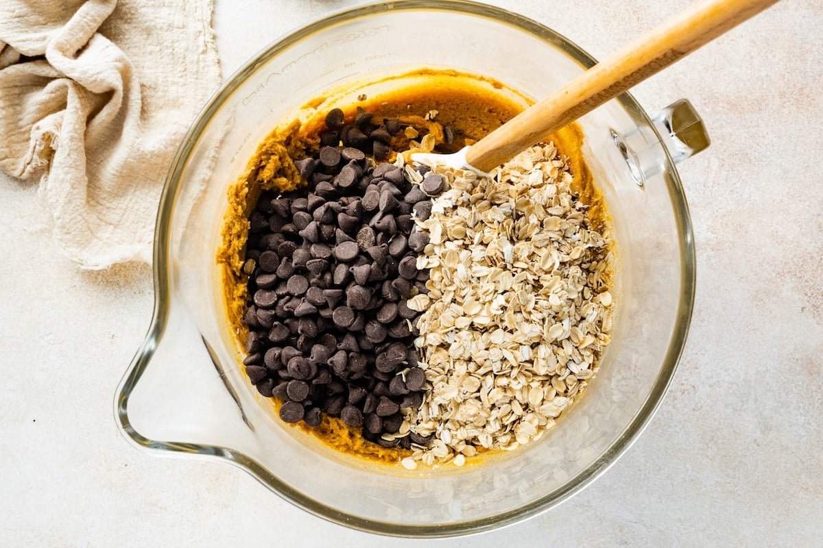 stirring in chocolate chips and oats to pumpkin cookie dough in mixing bowl with spatula.