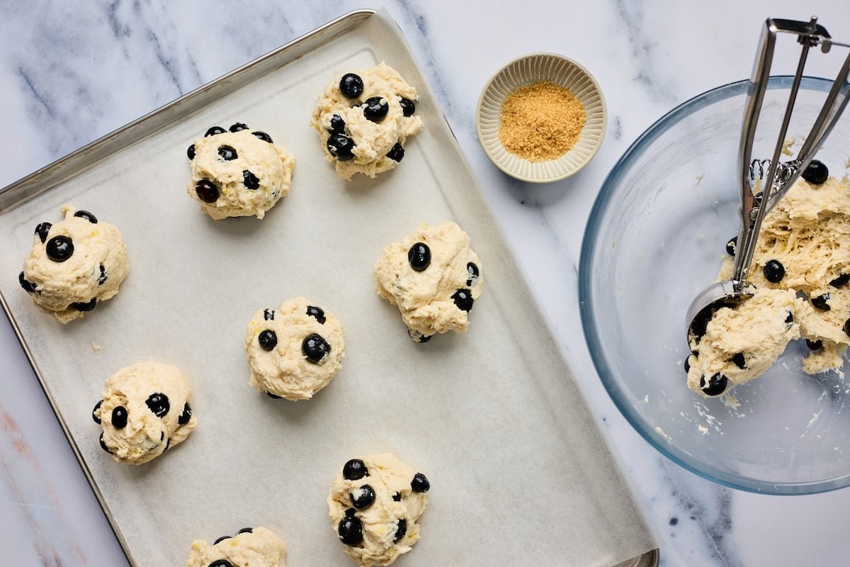 blueberry biscuits being scooped onto a baking sheet with parchment paper.