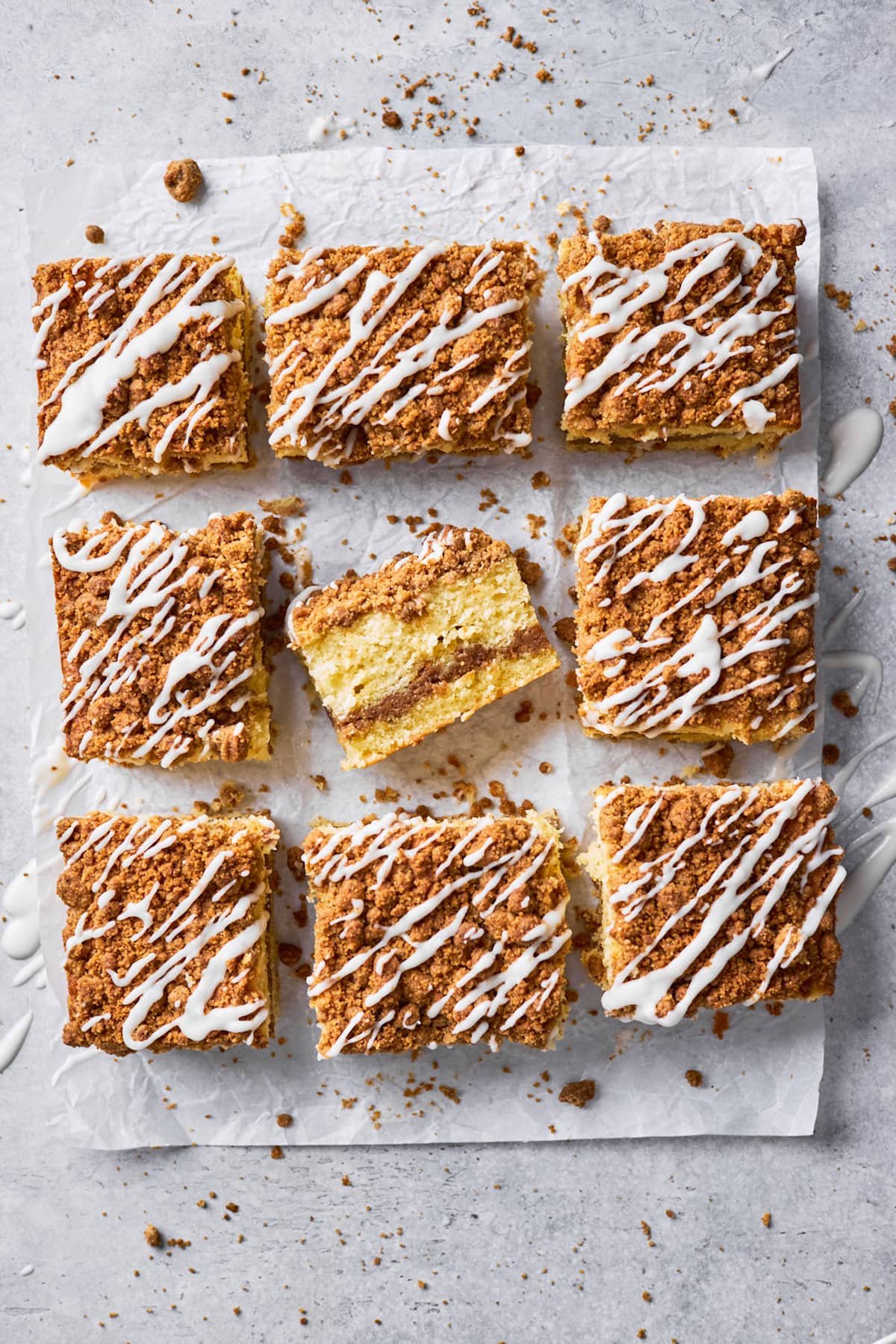 coffee cake with cinnamon streusel topping and vanilla glaze cut in squares on parchment paper.