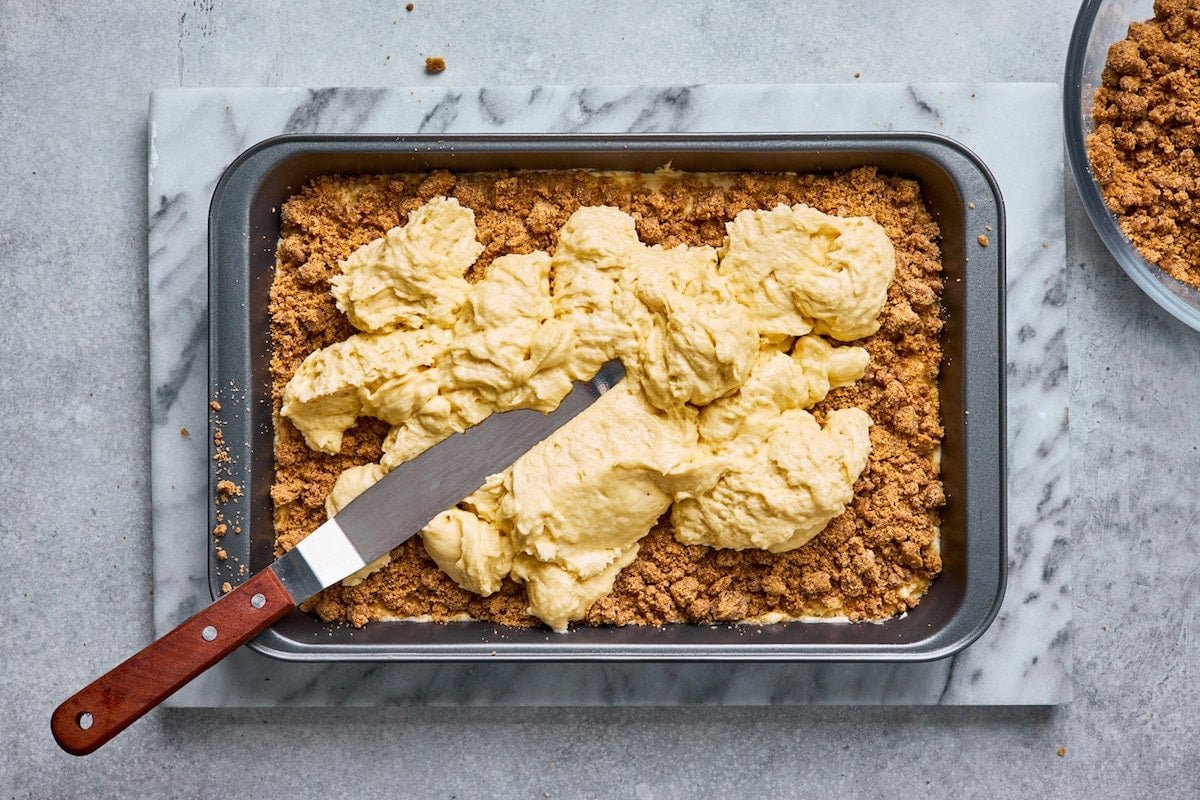 layering coffee cake batter and cinnamon streusel in baking pan with spatula.