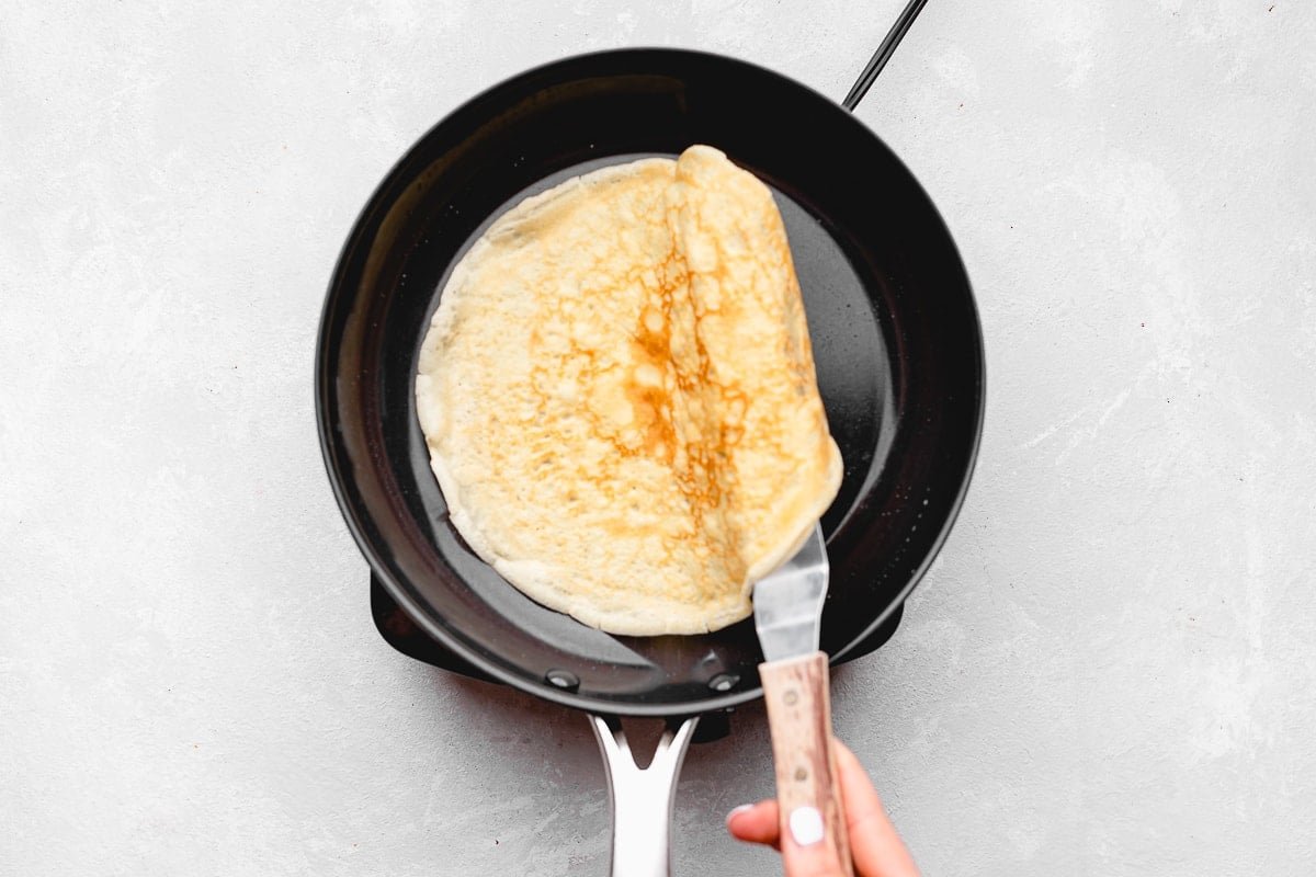 flipping crepe in skillet with a spatula.