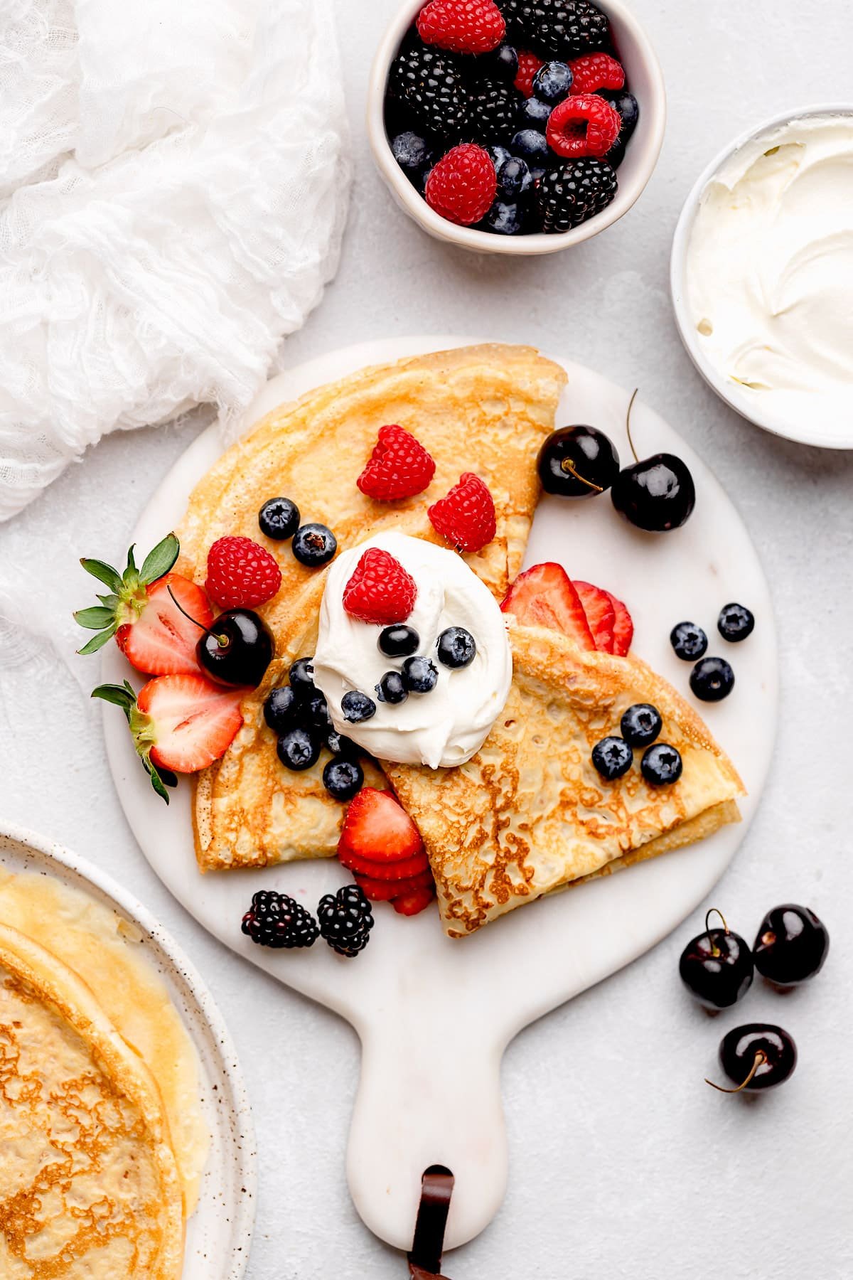 crepes on white marble board with berries and whipped cream.