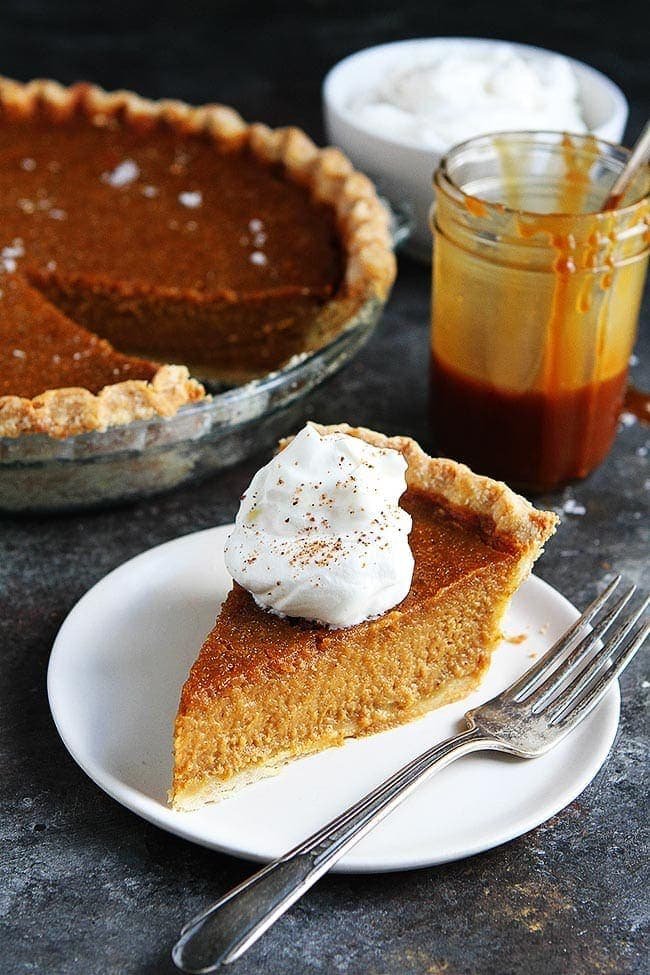 Salted Caramel Pumpkin Pie Is The BEST Pumpkin Pie Recipe. This Pumpkin Pie Will Be Everyone's Favorite Thanksgiving Dessert! #pumpkin #pumpkinpie #pie #pierecipe #Thanksgiving #Christmas #holidays #baking #Thanksgivingrecipe Piece of Salted Caramel Pumpkin Pie on plate with whipped cream and a fork.
