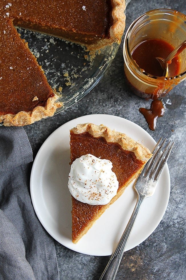 Salted Caramel Pumpkin Pie Is The BEST Pumpkin Pie Recipe. This Pumpkin Pie Will Be Everyone's Favorite Thanksgiving Dessert! #pumpkin #pumpkinpie #pie #pierecipe #Thanksgiving #Christmas #holidays #baking #Thanksgivingrecipe Overheat shot of a piece of Salted Caramel Pumpkin Pie with whipped cream on plate with a fork.
