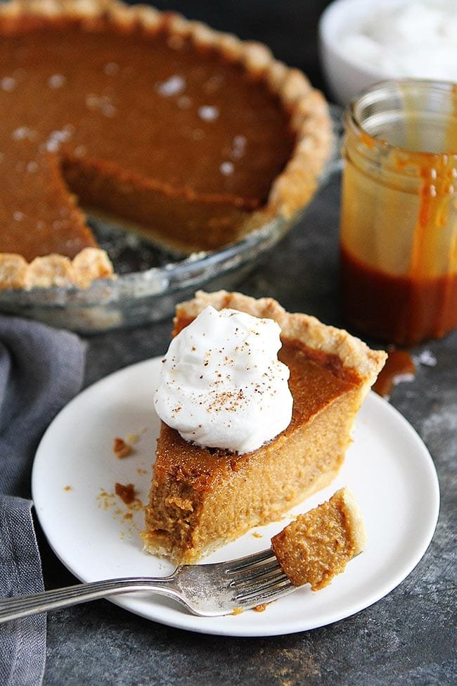 Salted Caramel Pumpkin Pie Is The BEST Pumpkin Pie Recipe. This Pumpkin Pie Will Be Everyone's Favorite Thanksgiving Dessert! #pumpkin #pumpkinpie #pie #pierecipe #Thanksgiving #Christmas #holidays #baking #Thanksgivingrecipe Salted caramel pumpkin pie on plate with a bite taken out of it with a fork.