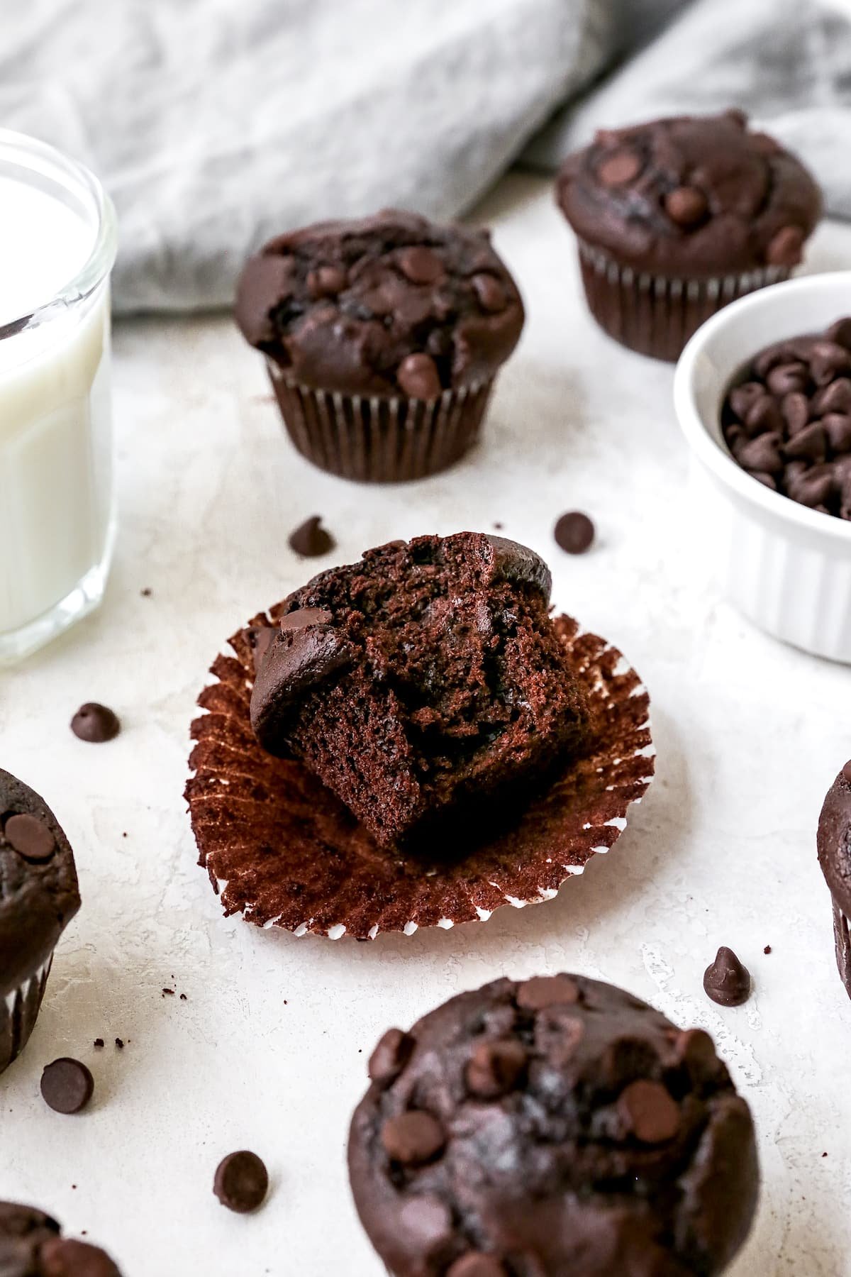 Chocolate muffin unwrapped with a bite taken out with milk and more muffins.